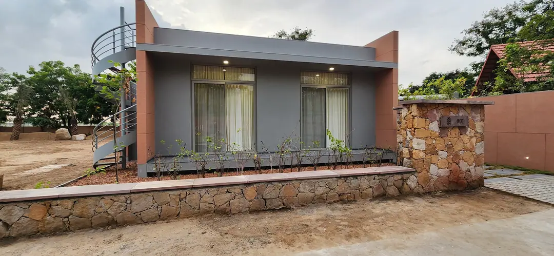 Grey single-storey farmhouse with two tall powder-coated aluminium sliding windows behind a stone boundary wall