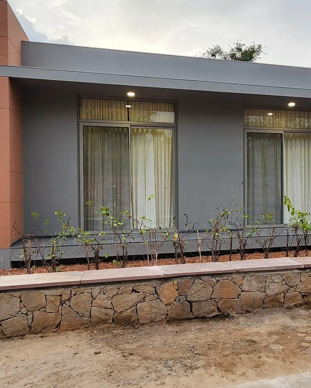 Grey single-storey farmhouse with two tall powder-coated aluminium sliding windows behind a stone boundary wall