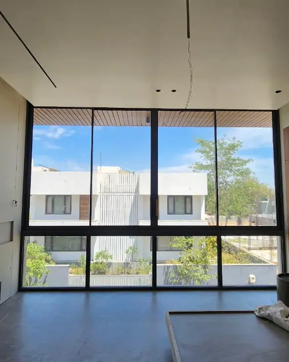Floor-to-ceiling glazing with slim black frames across a tall living space overlooking neighbouring houses