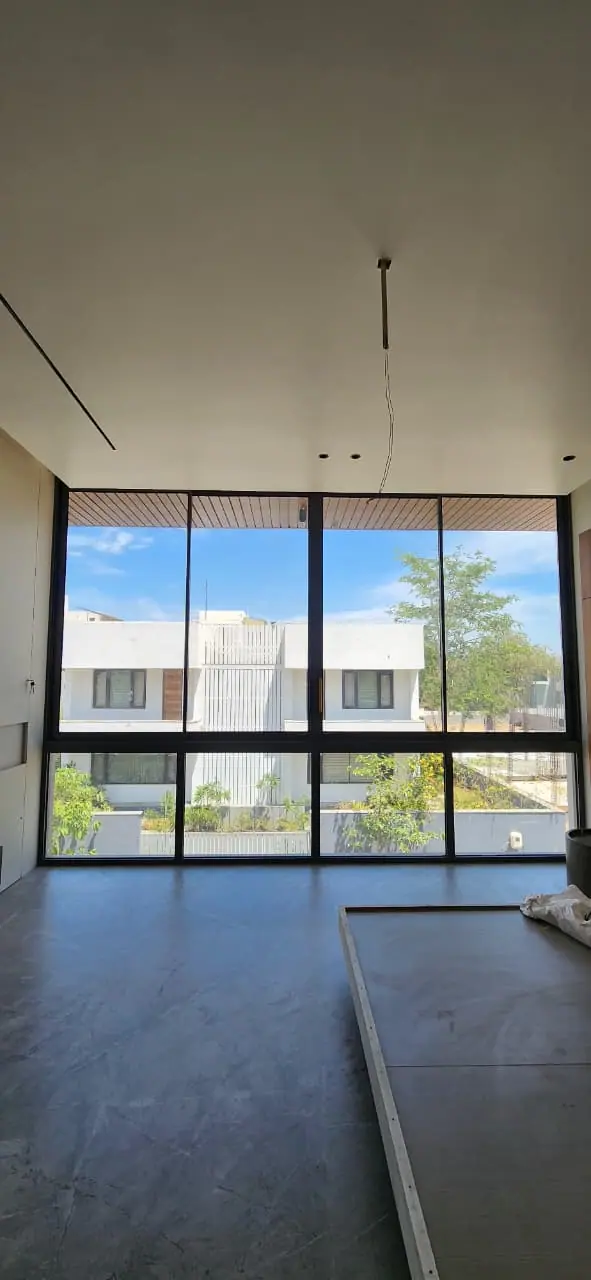 Floor-to-ceiling glazing with slim black frames across a tall living space overlooking neighbouring houses