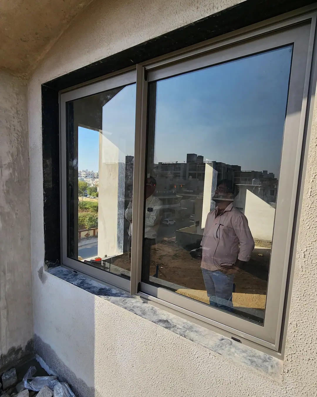 Newly fitted two-panel aluminium sliding window in a rendered wall, with a member of the fitting team reflected in the glass