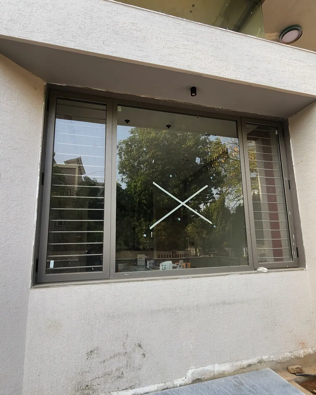 Grey aluminium sliding window with an insect mesh panel, fitted into the wall of a house under construction