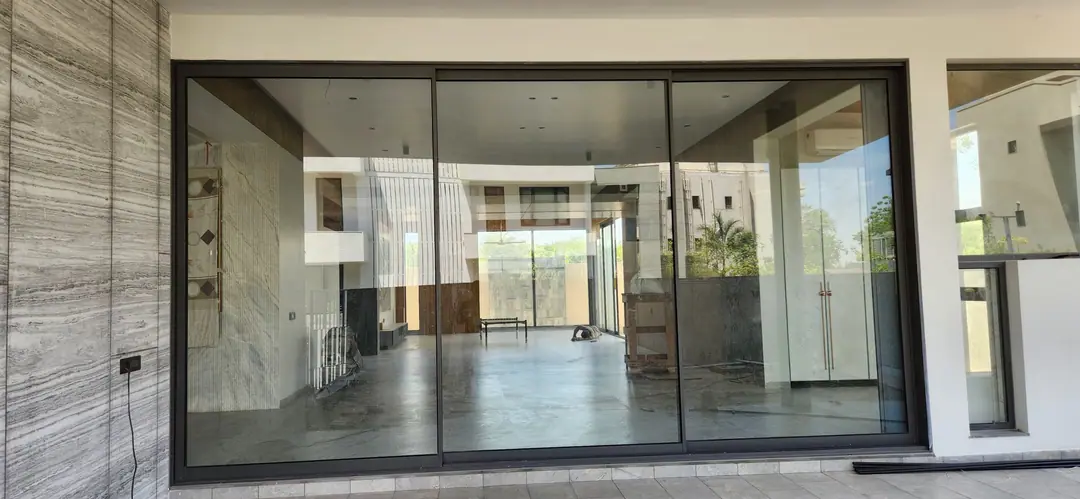 Slim-framed three-panel aluminium sliding doors set in a marble-clad wall, looking into a large interior